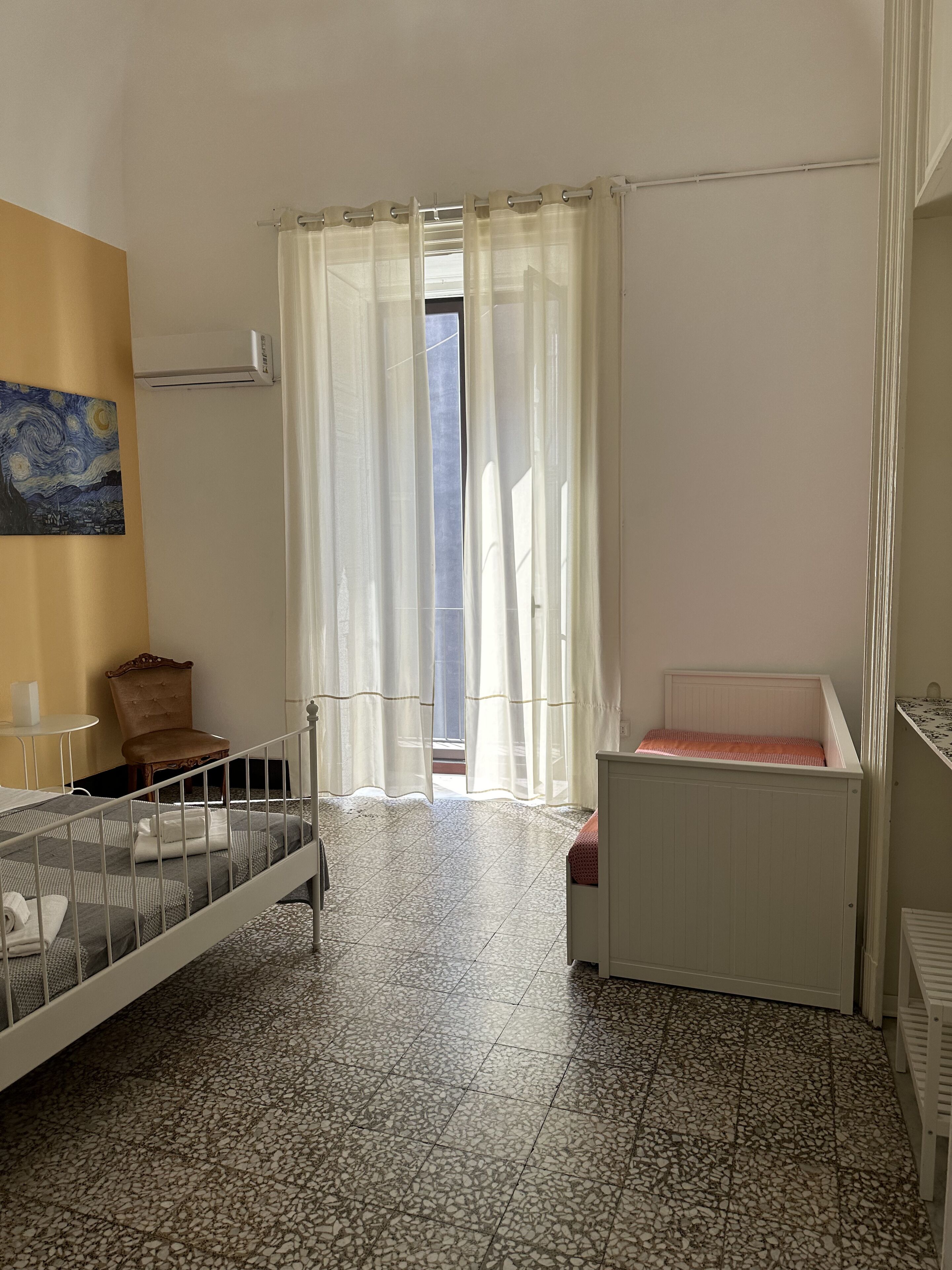 Un dormitorio con cama, una mesita, una silla, un radiador y un cuadro en la pared.