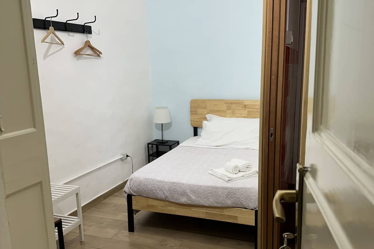 Um quarto com uma cama, uma mesa de cabeceira com abajur, um cabideiro e um aparelho de ar condicionado.
