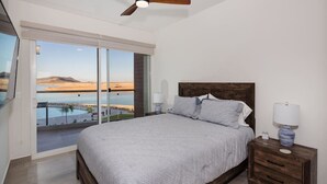 Een slaapkamer met een groot bed, een nachtkastje met een lamp en uitzicht op een zwembad en landschap door een schuifdeur.