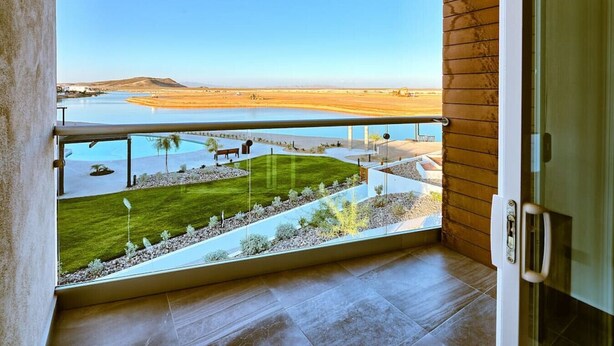 Een balkon met uitzicht op een aangelegde tuin en een waterpartij.