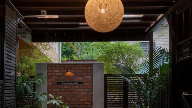 Un pasillo cubierto con luces esféricas colgantes, un muro de ladrillo con un letrero y plantas en macetas.