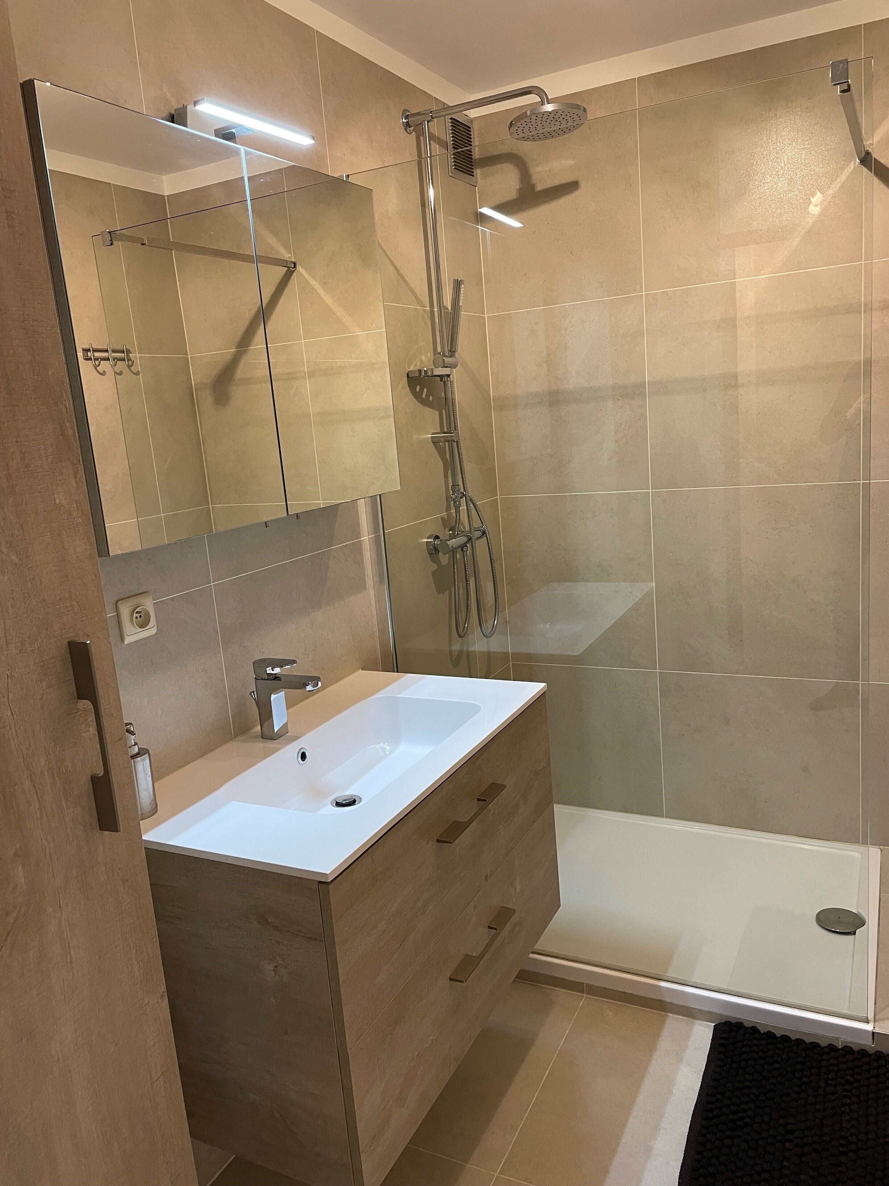 Ein modernes Badezimmer mit Duschkabine aus Glas, einem weißen Waschbecken und einem Holzbadezimmermöbel.