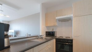 A modern kitchen with light wood cabinets, a black stove, a microwave, and a coffee maker. - Modern apartment with beautiful sea view! (Blankenberge)