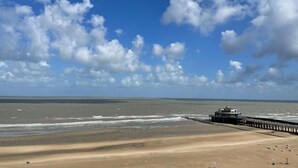 A beach with a pier extending into the ocean, a clear sky, and a sandy shore. - Modern apartment with beautiful sea view! (Blankenberge)