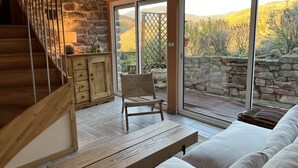 Un interior moderno con una escalera de madera, un muro de piedra, un banco de madera, un sofá blanco y vistas a un jardín a través de amplios ventanales correderas.