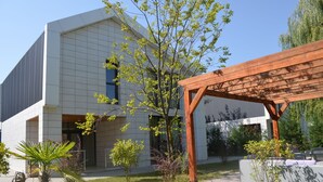 A modern building with a white facade, a wooden pergola, and a small garden area with various plants. - Arena Villas Guba (Quba)