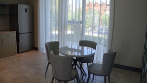 A compact kitchen with a refrigerator, a dining table with four chairs, and a large window with sheer curtains. - Arena Villas Guba (Quba)