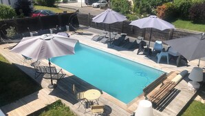 A rectangular swimming pool with a wooden deck surrounding it, equipped with lounge chairs, umbrellas, and a small table. - La Petite Maison Sous le Toit - 25 km Nord de Strasbourg (Kriegsheim)