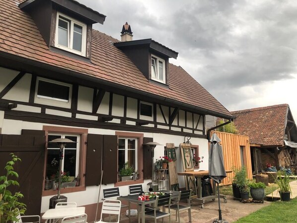 Een traditioneel vakwerkhuis met een schuin dak, een klein balkon en een terras met tuinmeubilair.