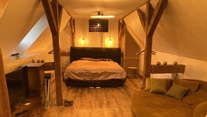 A bedroom with a bed, wooden beams, a small table, and a sofa. - La Petite Maison Sous le Toit - 25 km Nord de Strasbourg (Kriegsheim)