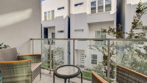 A balcony with wicker furniture, a glass table, and a view of a modern building with multiple windows. - Luxurious Houston NRG/Medical Center Townhome (Houston)
