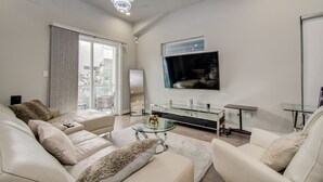 A modern living room with a sofa, a glass coffee table, and a TV mounted on the wall. - Luxurious Houston NRG/Medical Center Townhome (Houston)