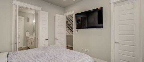 A bedroom with a bed, a TV mounted on the wall, and a staircase leading to a closet.