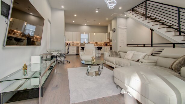 A modern living room with a glass coffee table, a white sofa, and a staircase with a black railing. - Luxurious Houston NRG/Medical Center Townhome (Houston)
