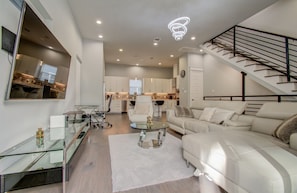 A modern living room with a glass coffee table, a white sofa, and a staircase with a black railing. - Luxurious Houston NRG/Medical Center Townhome (Houston)