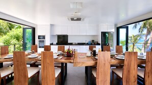 A modern dining area with wooden chairs and tables, white cabinets, and a view of the outdoors. - Room B8 - PANORAMIC SEA VIEW (Koh Samui)