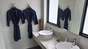 A modern bathroom with two sinks, a large mirror, and two dark blue robes hanging on hooks. - Room B8 - PANORAMIC SEA VIEW (Koh Samui)