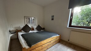 Camera da letto con un letto di legno, pareti bianche, un quadro incorniciato e una finestra vista verde.