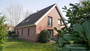 Una casa a due piani in mattoni con tetto spiovente, un piccolo giardino antistante e una finestra ben visibile.