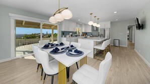 Une cuisine moderne avec des meubles blancs, un îlot central et un coin repas comprenant des chaises blanches et une table dressée pour quatre personnes.