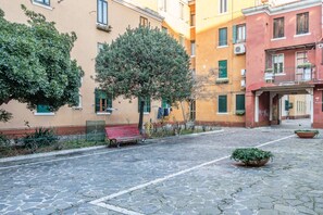 Une cour pavée avec un banc, des plantes en pot et des immeubles à plusieurs étages dotés de balcons.