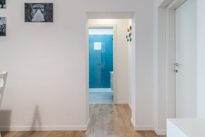 Un couloir avec un plancher en bois, une porte blanche et un mur recouvert de carreaux bleus.