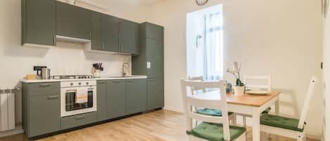 Une cuisine équipée d’une cuisinière, d’un four et de placards, une table à manger avec des chaises, et une fenêtre avec des rideaux.