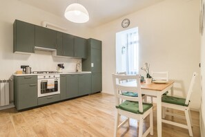 Une cuisine équipée d’une cuisinière, d’un four et de placards, une table à manger avec des chaises, et une fenêtre avec des rideaux.