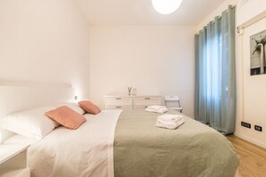 Un dormitorio ordenado con cama, mesitas de noche, cómoda y ventana con cortinas.