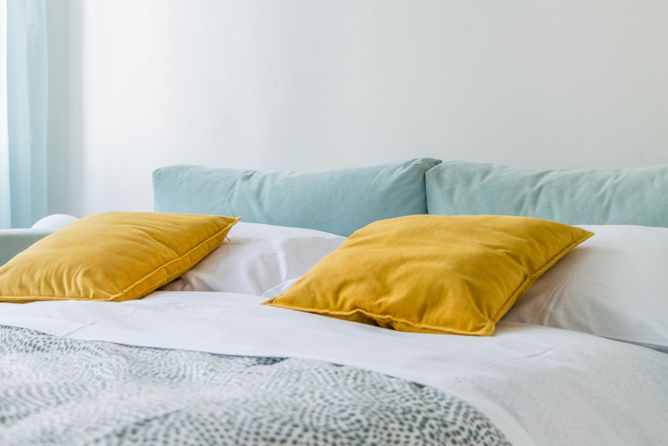 A bed with white bedding and two mustard yellow pillows.