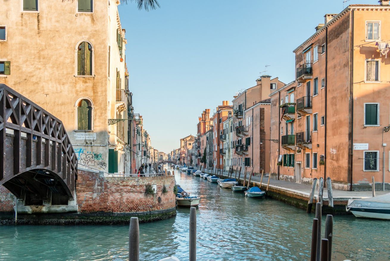 A canal with buildings on either side, a bridge, and boats docked along the water.
