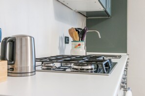 Una cocina con estufa a gas, hervidor y un organizador de utensilios sobre la encimera.