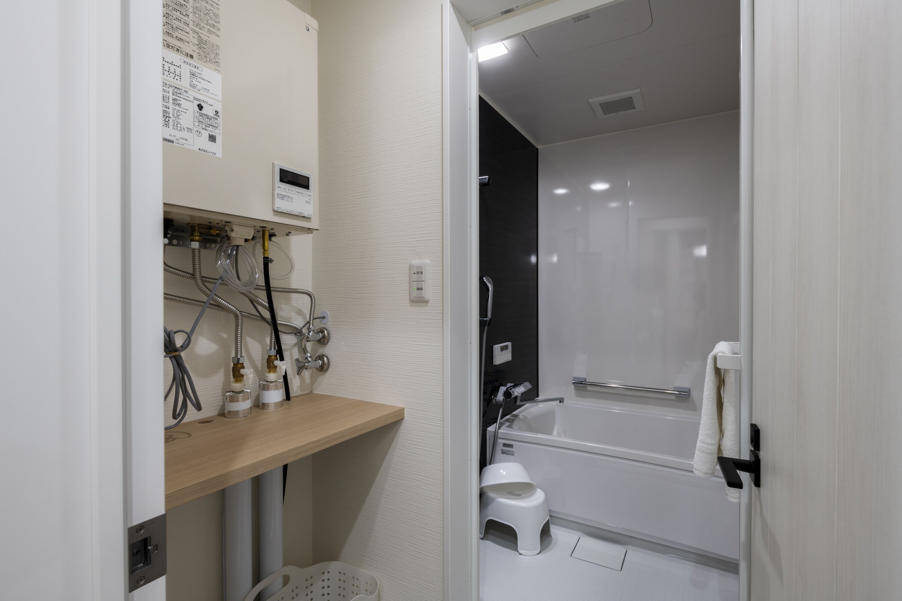 A modern bathroom with a bathtub, a small stool, and a wooden shelf with various toiletries.
