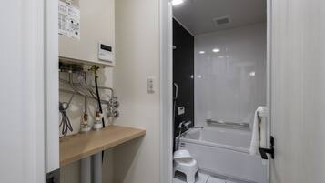 A modern bathroom with a bathtub, a small stool, and a wooden shelf with various toiletries.