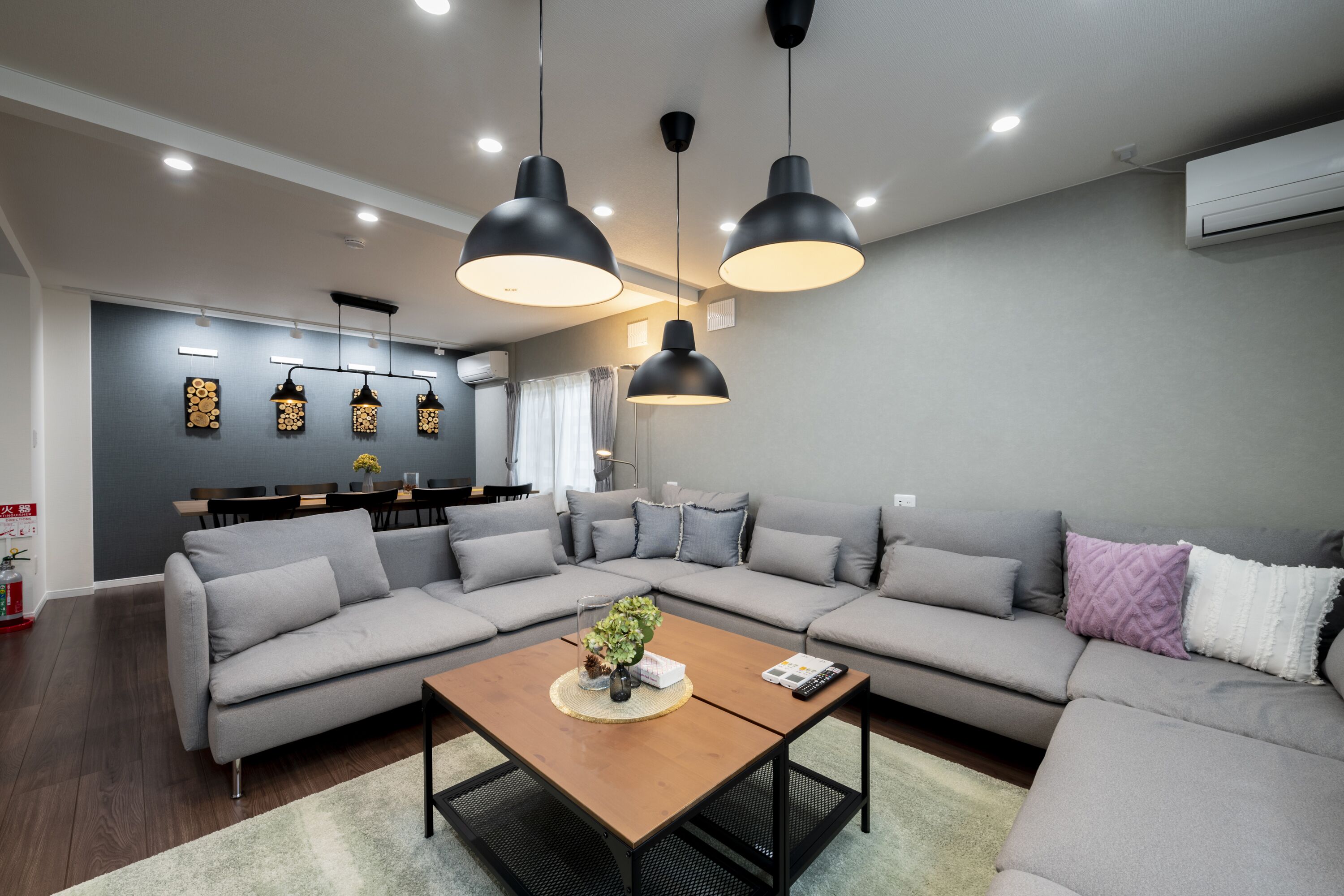 Una sala de estar moderna con un sofá seccional, una mesa de centro de madera e iluminación colgante.
