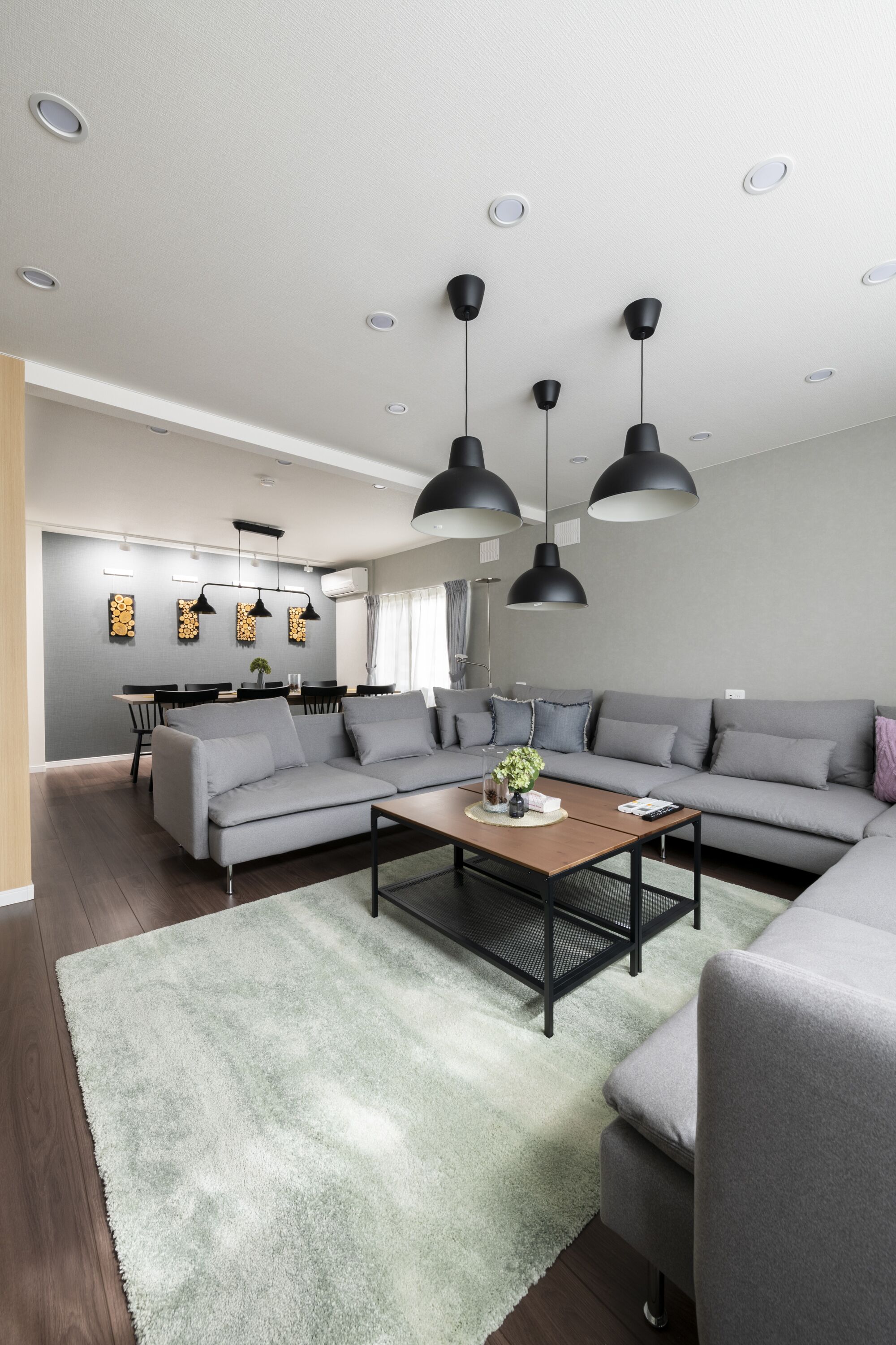 A modern living room with a grey sofa, a wooden coffee table, and black pendant lights.