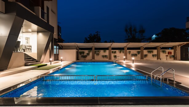 An indoor swimming pool with a modern design, surrounded by a building with a staircase and a covered area. - Regenta Place Igatpuri  (Igatpuri)