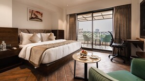 A hotel room with a large bed, a dining table with breakfast, a desk, and a view of the city through the balcony. - Regenta Place Igatpuri  (Igatpuri)