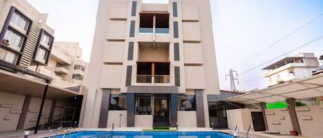 Un immeuble moderne à plusieurs étages, avec une piscine située devant.