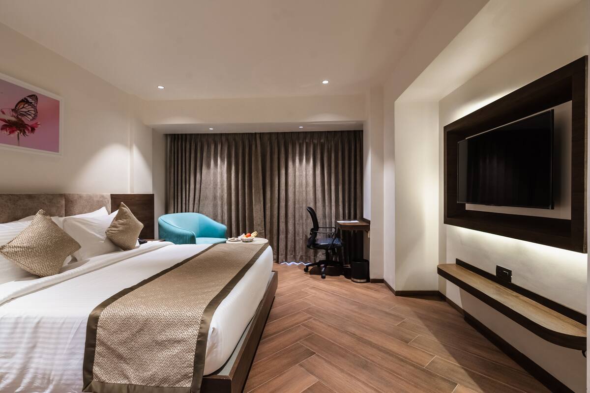 A hotel room with a large bed, a desk, a chair, a TV, and a curtain.