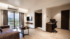 A modern living room with a sofa, a coffee table, and a TV mounted on the wall. There is a desk with a chair and a wooden shelf above it. - Regenta Place Igatpuri  (Igatpuri)
