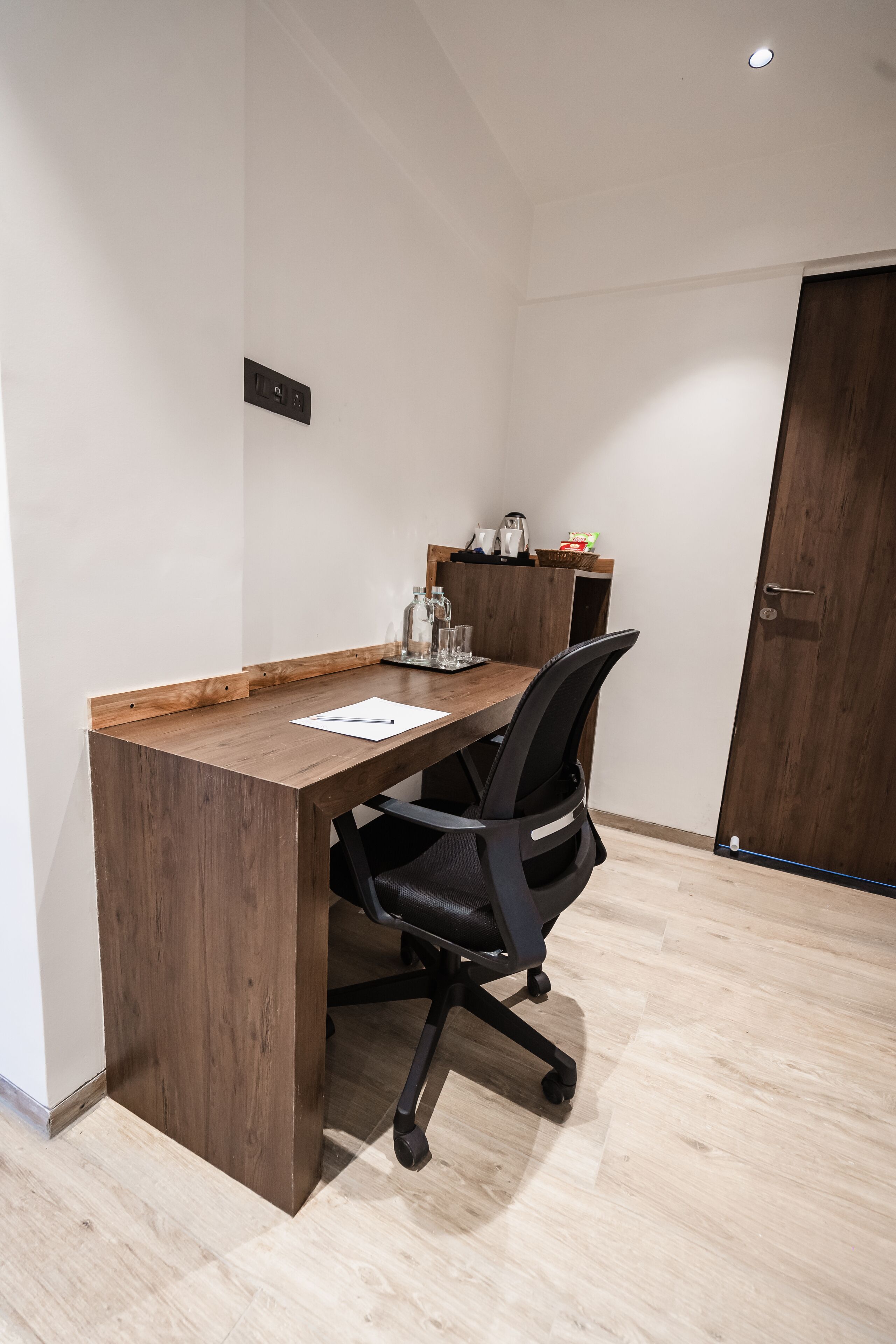 A small office with a wooden desk, a black office chair, a whiteboard, and a coffee machine.