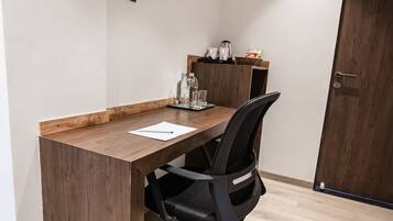 Un petit bureau avec un bureau en bois, un fauteuil de bureau noir, un tableau blanc et une machine à café.