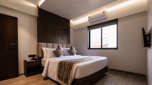 A modern bedroom with a large bed, a nightstand, a wooden floor, and a window with a view. - Regenta Place Igatpuri  (Igatpuri)