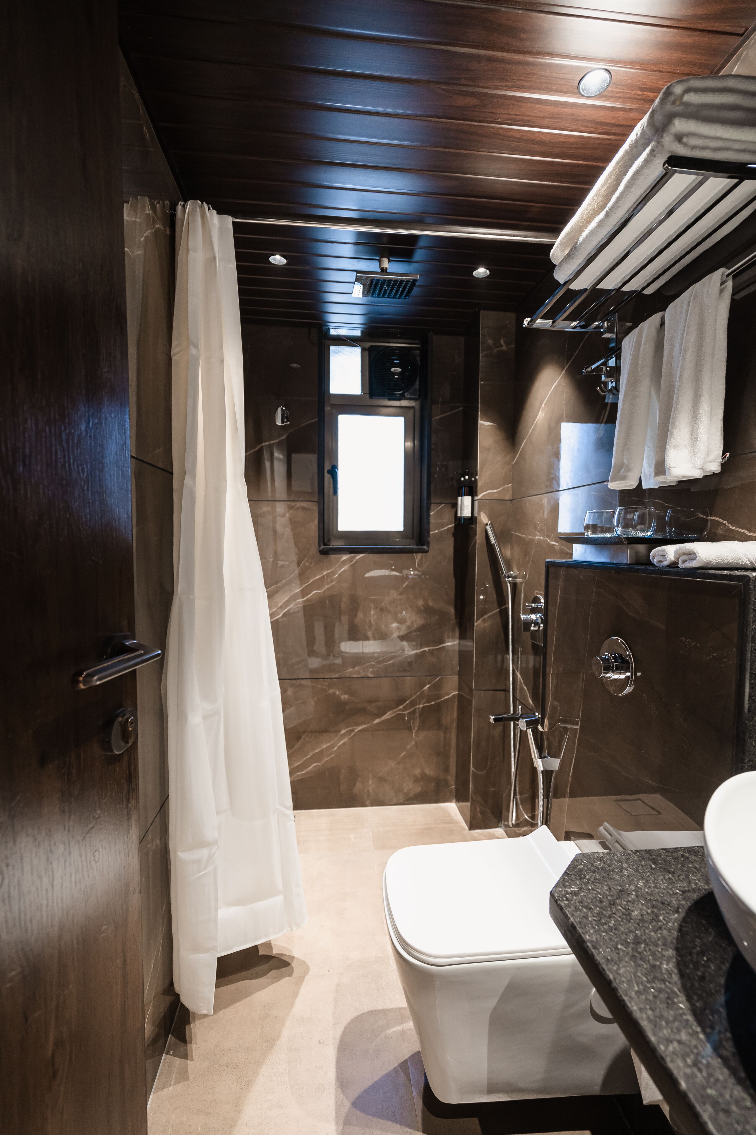 A modern bathroom with a marble floor, a white toilet, a shower with a glass enclosure, and a vanity with a mirror and towel rack.