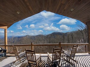 Une terrasse en bois avec quatre chaises et une table en bois, offrant une vue sur un paysage montagneux sous un ciel dégagé.
