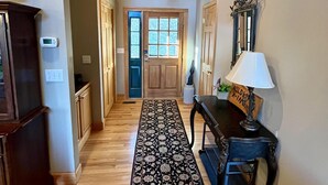 A hallway with wooden flooring, a patterned rug, a wooden ceiling, a door with glass panels, a table with a lamp, and a cabinet.