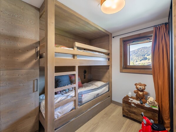 A bunk bed room with wooden walls, a window with a view, and a dresser with stuffed animals. - Luxurious Apartment for 6 with Spa Access in Peaceful Rochebrune (Megève)