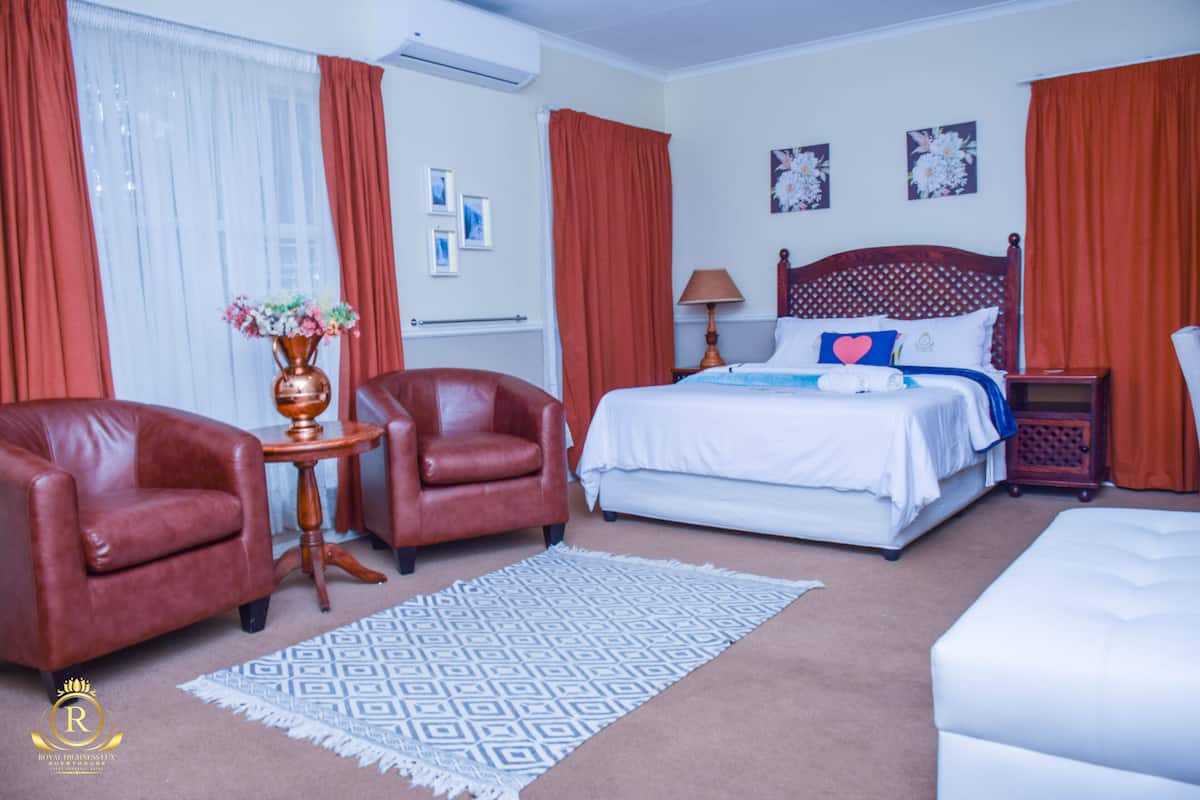 Een hotelkamer met een bed, twee leren fauteuils, een klein tafeltje met een vaas, een kamerkleed met patroon en een nachtkastje met een lamp.