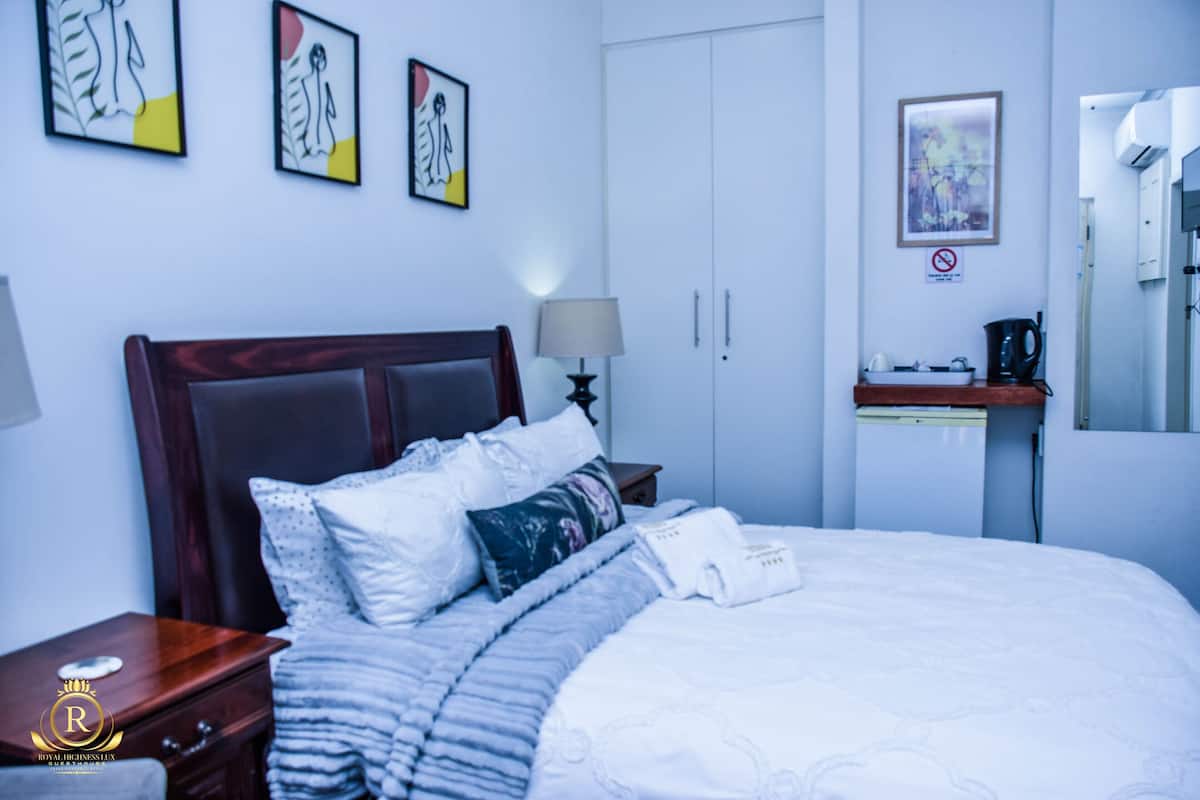Een hotelkamer met een bed, nachtkastje, lamp, kledingkast en kunst aan de muren.